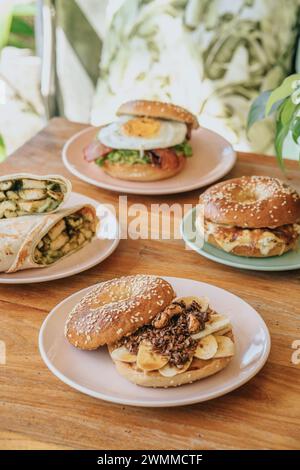 Un burrito e un hamburger di bagel su un piatto diviso con salsa verde, panna acida, vegano e pollo su un tavolo di legno Foto Stock