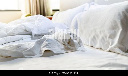 I cuscini bianchi con la coperta sul letto non erano fatti, il letto era disordinato Foto Stock