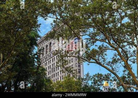 La bandiera americana e il Flatiron Building visti dagli alberi del Madison Square Park - Manhattan, New York City Foto Stock