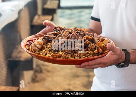 Cibo nazionale - pilaf uzbeko con carne in piatto con schema tradizionale. il cameriere consegna il pilaf nel ristorante Foto Stock