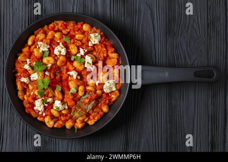 plaki gigantes, fagioli giganti greci al forno in una grossa salsa di pomodoro cosparsa di feta e coriandolo fresco su una padella su un tavolo di legno nero, horiz Foto Stock