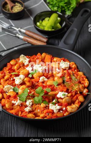 plaki gigantes, fagioli giganti greci al forno in una grossa salsa di pomodoro cosparsa di feta e coriandolo fresco su una padella su un tavolo di legno nero con Foto Stock