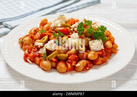 plaki di gigantes, fagioli giganti greci al forno in una grossa salsa di pomodoro cosparsa di feta, olive e prezzemolo fresco sul piatto su un tavolo di legno bianco, Foto Stock