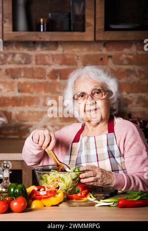 Donna anziana che cucina insalata di verdure in cucina a casa Foto Stock