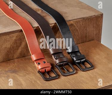 Tre cinture in vera pelle di diversi colori con fibbie in metallo e PAPÀ in rilievo sul supporto in legno. Elegante artigianato personalizzato Foto Stock
