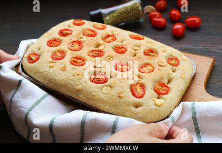 Mettere a mano il pane con focaccia all'aglio e il pomodoro italiano appena sfornato su una bacheca di legno Foto Stock