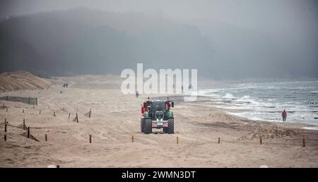 Rostock, Germania. 27 febbraio 2024. Sulla spiaggia di Warnemünde, un trattore raccoglie sabbia dalla zona del molo occidentale e la riporta a ovest. Ogni anno, il vento soffia diverse tonnellate di sabbia sulla spiaggia della località balneare del Baltico. Le tempeste di inizio gennaio in particolare hanno contribuito a questo. Crediti: Frank Hormann/dpa/Alamy Live News Foto Stock