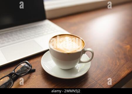 Una tazza di caffè si trova vicino a un computer portatile su un tavolo di legno con spazio per le copie Foto Stock