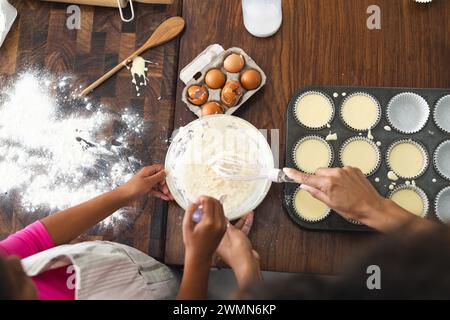 Madre e figlia birazziali che cucinano insieme a casa per figlia. Stanno preparando cupcake, creando un'attività culinaria divertente ed educativa. Foto Stock