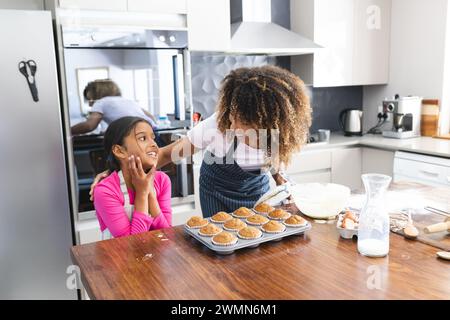 Madre e figlia birazziali si divertono a cucinare insieme a casa per figlia. Condividono un momento dolce in un ambiente accogliente in cucina. Foto Stock