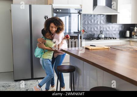 La madre birazziale abbraccia la figlia birazziale in una cucina moderna. Condividono un caldo abbraccio, mettendo in risalto un ambiente domestico di cura per la figlia. Foto Stock