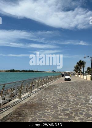 Una panchina su una passerella sul mare con uno sfondo urbano Foto Stock