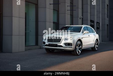 Bentley Bentayga ha parcheggiato vicino all'entrata di un edificio moderno - vista frontale di tre quarti del SUV di lusso al tramonto vicino al centro affari. Foto Stock