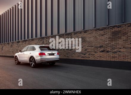 Bentley Bentayga ha parcheggiato vicino alle pareti in mattoni di un edificio moderno - vista posteriore di tre quarti del SUV di lusso al tramonto. Foto Stock