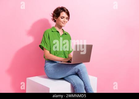 Ritratto di una ragazza di grande successo seduto sul podio utilizzare la rete wireless del laptop isolata su sfondo rosa Foto Stock