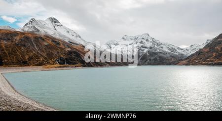 Serbatoio con acqua turchese nelle Alpi Silvretta. Montagne arrugginite innevate in una giornata nuvolosa. Foto Stock