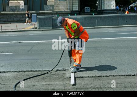 Lavoratore che prepara la posa per asfaltare la strada su strada utilizzando un demolitore pneumatico. 7 agosto 2021. Kiev, Ucraina Foto Stock