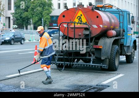 Lavoratore che asfalta ripara la strada su strada utilizzando una macchina spruzzatrice bitume. 7 agosto 2021. Kiev, Ucraina Foto Stock