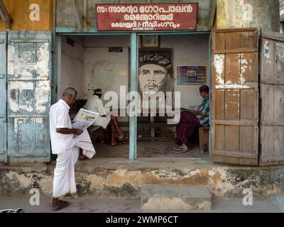India, kerala, Kochi: Gli uomini indiani leggono il giornale in un ufficio pubblico del Partito Comunista del Kerala con l'immagine di che Gevara Foto Stock