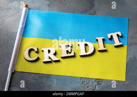 Testo da lettere di legno e bandiera Ucraina su sfondo astratto, concetto sul tema del credito in Ucraina Foto Stock
