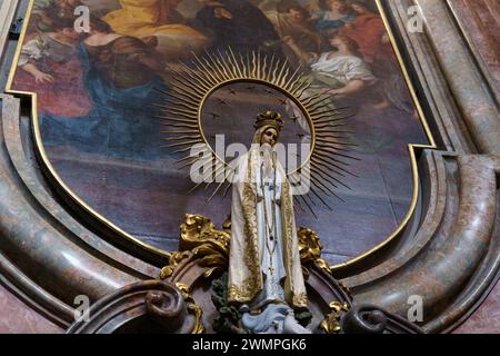 Poznan, Polonia - 18 giugno 2023: Una statua della Vergine Maria si erge di fronte a un dipinto religioso, creando una suggestiva scena religiosa. Foto Stock