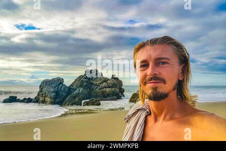 L'uomo viaggiatore Turistico maschile realizza Selfie con le splendide rocce scogliere pietre massi e enormi onde surfisti e vista panoramica naturale sulla spiaggia in Foto Stock