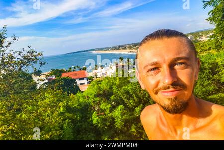 L'uomo viaggiatore Turistico maschile realizza Selfie con le splendide rocce scogliere pietre massi e enormi onde surfisti e vista panoramica naturale sulla spiaggia in Foto Stock