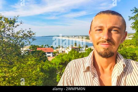 L'uomo viaggiatore Turistico maschile realizza Selfie con le splendide rocce scogliere pietre massi e enormi onde surfisti e vista panoramica naturale sulla spiaggia in Foto Stock