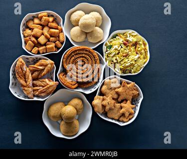 Foto ravvicinata di spuntini Diwali freschi assortiti o faral riempiti di ciotole bianche con uno sfondo nero chiaro. Foto Stock