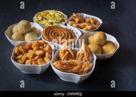 Foto ravvicinata di spuntini assortiti, freschi Diwali o faral riempiti di ciotole bianche con uno sfondo nero chiaro. Foto Stock