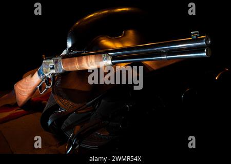 Sfondo scuro dietro la sella e il fucile a leva con illuminazione arancione del bordo. Foto Stock