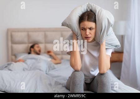 Donna frustrata dal russare, coprendo le orecchie con il cuscino Foto Stock