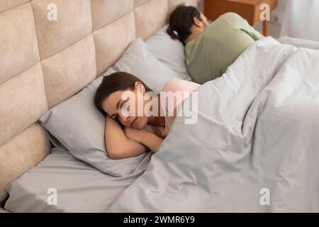 Donna sconvolta sdraiata a letto con la schiena all'uomo Foto Stock