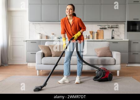 Donna sorridente che usa un aspirapolvere rosso in una cucina moderna Foto Stock