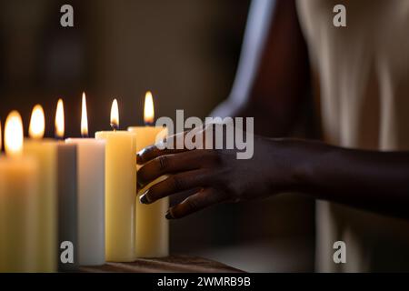 Primo piano non riconoscibile donna afroamericana sconosciuta donna ragazza femminile mani che toccano fila di luci molte alte candele di cera comodino o tavolo da massaggio Foto Stock