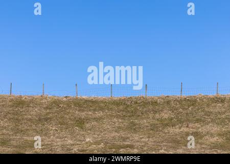 Recinzione sulla cima di una collina erbosa con un cielo azzurro pulito. Foto Stock