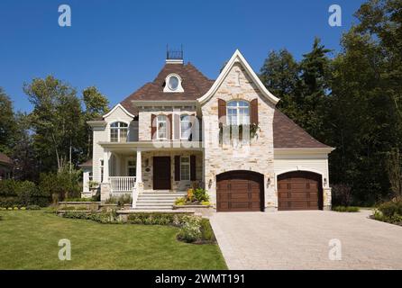 Lussuosa casa a due piani con abbronzatura marrone e pietra tagliata con due garage per auto, giardino panoramico e vialetto di pietra in pavimentazione in estate. Foto Stock