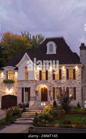 Lussuosa casa illuminata a due piani in pietra marrone tagliata con giardino panoramico in estate al tramonto. Foto Stock