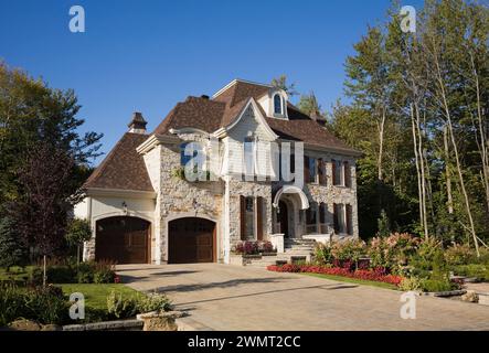 Lussuosa casa a due piani con abbronzatura marrone e pietra tagliata con due garage per auto, vialetto di pietra e giardino panoramico in estate. Foto Stock