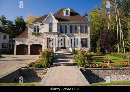 Lussuosa casa a due piani con abbronzatura marrone e pietra tagliata con due garage per auto, vialetto di pietra e giardino panoramico in estate. Foto Stock