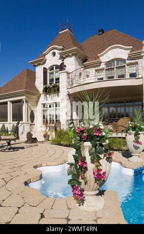 Piscina interna con spa nel cortile posteriore di lussuosa casa di pietra di colore chiaro a due piani con giardino paesaggistico sul retro in estate. Foto Stock