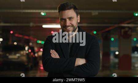 Ritratto sorridente uomo d'affari caucasico boss uomo adulto in posa braccia incrociate posa in garage sotterraneo parcheggio fiducioso Guy venditore di auto autista di Foto Stock