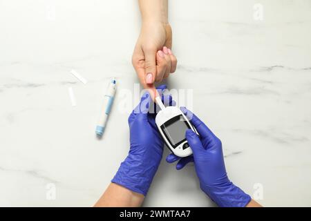 Diabete. Medico che controlla il livello di zucchero nel sangue del paziente con il glucometro sul tavolo in marmo bianco, vista dall'alto Foto Stock