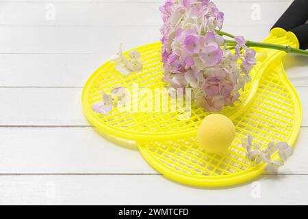 Composizione con racchette da tennis, palla e fiori su sfondo di legno chiaro. Giornata internazionale della donna Foto Stock