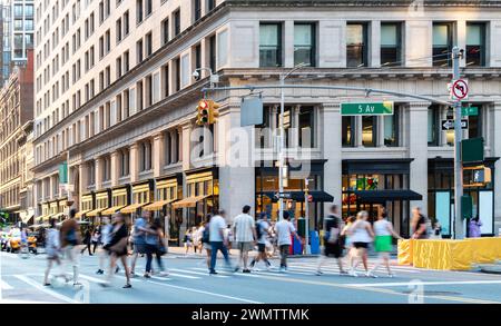 Folle di persone in movimento che camminano attraverso la trafficata intersezione tra la 5th Avenue e la 23rd Street a New York City NYC Foto Stock