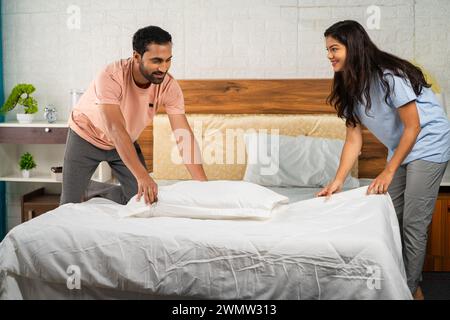 Coppia indiana che prepara o prepara il letto dopo il risveglio al mattino - concetto di rapporto gioioso, supporto di partnership e routine quotidiana. Foto Stock
