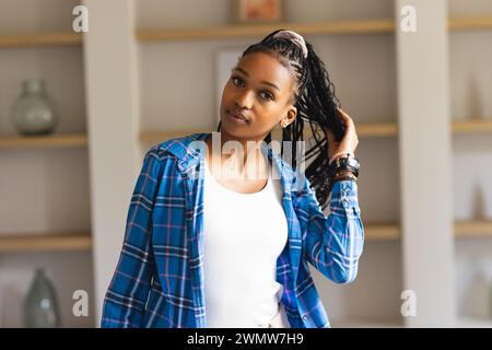 Una giovane donna afro-americana posa con fiducia, mano nei capelli intrecciati Foto Stock