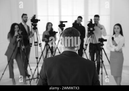 Uomo d'affari che fa un colloquio ai giornalisti al chiuso, vista posteriore. Effetto bianco e nero Foto Stock