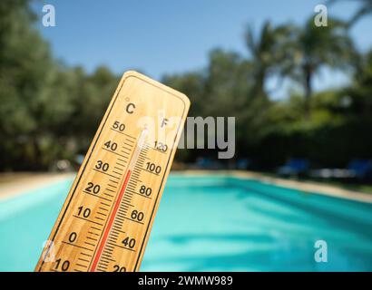 Termometro in legno con liquido di misurazione rosso che mostra temperature elevate nelle giornate di sole sullo sfondo della piscina. Concetto di vacanza, vacanza, caldo Foto Stock