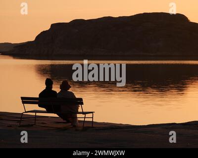 Una coppia seduta su una panchina che guarda il mare al tramonto Foto Stock